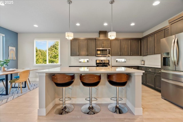 kitchen featuring hanging light fixtures, stainless steel appliances, an island with sink, dark brown cabinetry, and sink