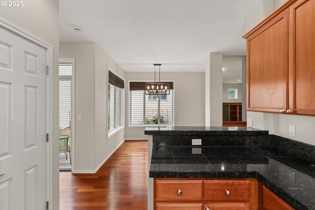 16044 SW Langer Dr, Sherwood, OR 97140 - kitchen with dark wood finished floors, a chandelier, brown cabinetry, a peninsula, and decorative light fixtures