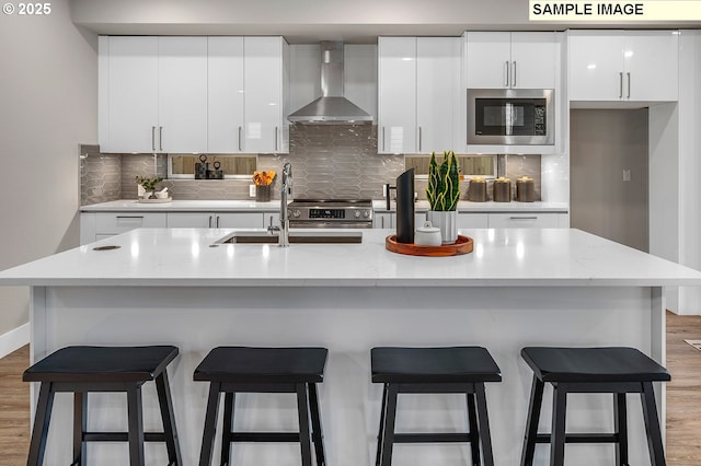 kitchen with a sink, stainless steel appliances, modern cabinets, and wall chimney exhaust hood