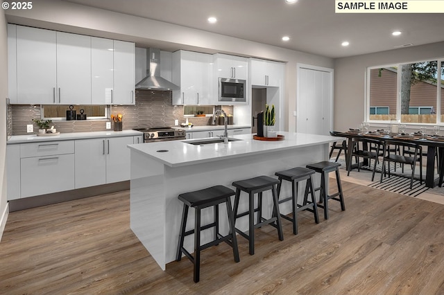 kitchen featuring a breakfast bar area, appliances with stainless steel finishes, modern cabinets, wall chimney exhaust hood, and a sink