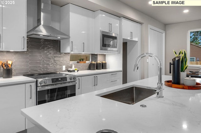 kitchen with a sink, decorative backsplash, white cabinets, appliances with stainless steel finishes, and wall chimney exhaust hood