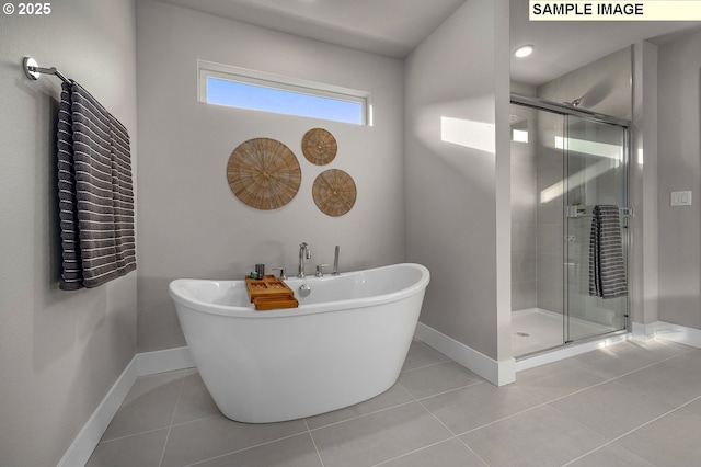 full bathroom featuring tile patterned flooring, a shower stall, a freestanding tub, and baseboards