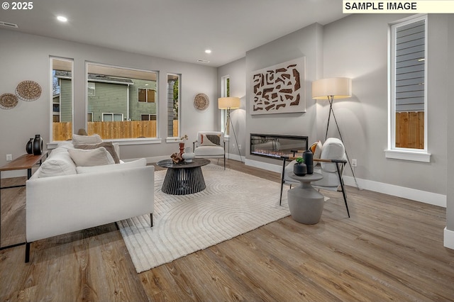 living area with a glass covered fireplace, recessed lighting, wood finished floors, and baseboards