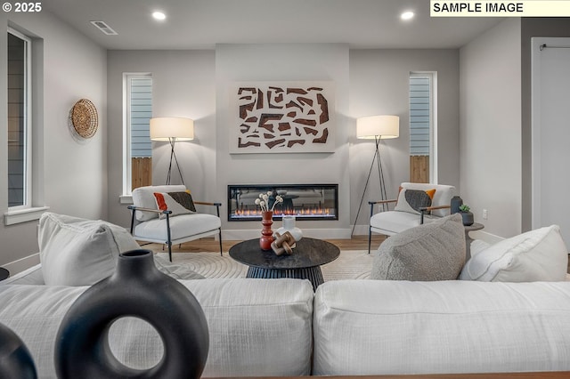 living room with recessed lighting, visible vents, wood finished floors, and a glass covered fireplace