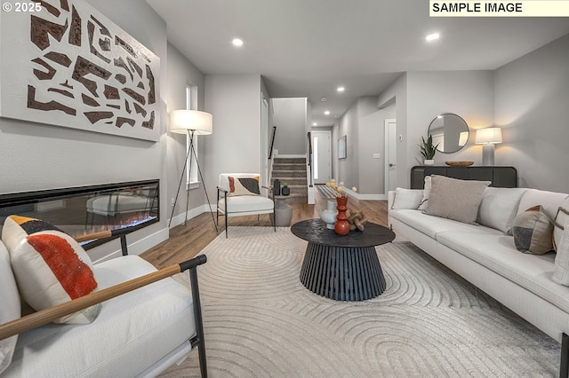 living room featuring wood finished floors, a glass covered fireplace, recessed lighting, baseboards, and stairs