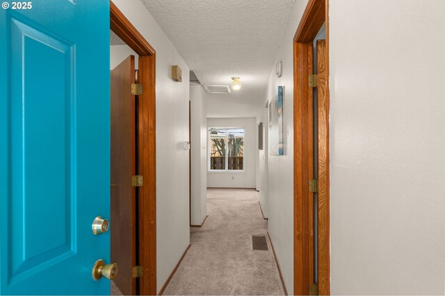 hallway featuring visible vents, light carpet, a textured ceiling, and baseboards