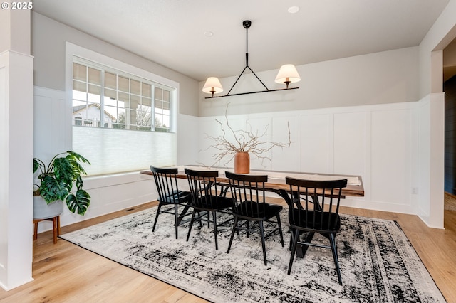 dining space with light wood-style floors, a chandelier, wainscoting, and a decorative wall