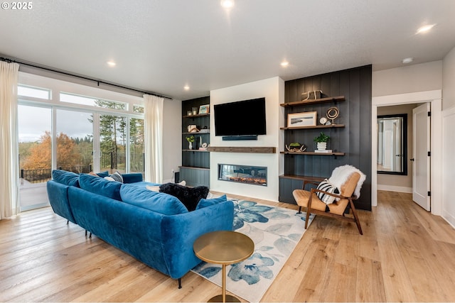 living area with light wood finished floors, built in shelves, recessed lighting, a glass covered fireplace, and a textured ceiling