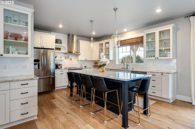 kitchen with light wood-type flooring, a breakfast bar, a sink, stainless steel appliances, and wall chimney exhaust hood