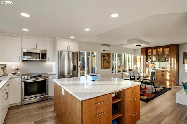 kitchen with white cabinetry, stainless steel appliances, a center island, a wall mounted AC, and light wood-type flooring