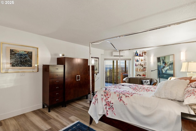 bedroom with a wall mounted AC, access to outside, and light hardwood / wood-style flooring