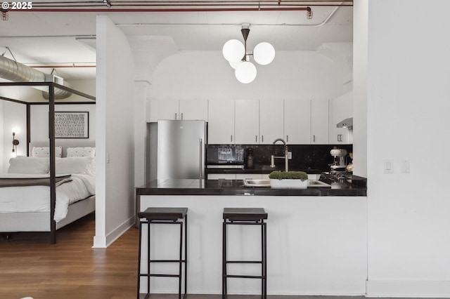 kitchen with a peninsula, freestanding refrigerator, backsplash, white cabinets, and dark countertops