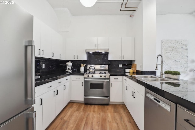 kitchen with a sink, tasteful backsplash, light wood-style flooring, dark countertops, and appliances with stainless steel finishes