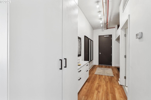 corridor with light wood finished floors, visible vents, and baseboards