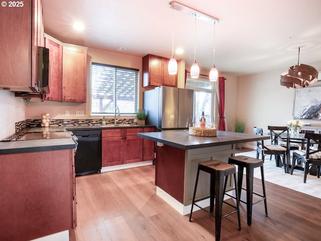 kitchen featuring sink, decorative light fixtures, a center island, light wood-type flooring, and black appliances