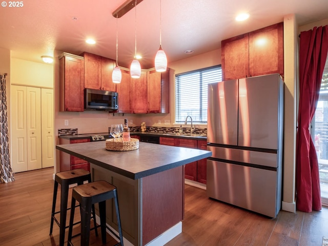 kitchen with a kitchen bar, sink, hanging light fixtures, a kitchen island, and stainless steel appliances