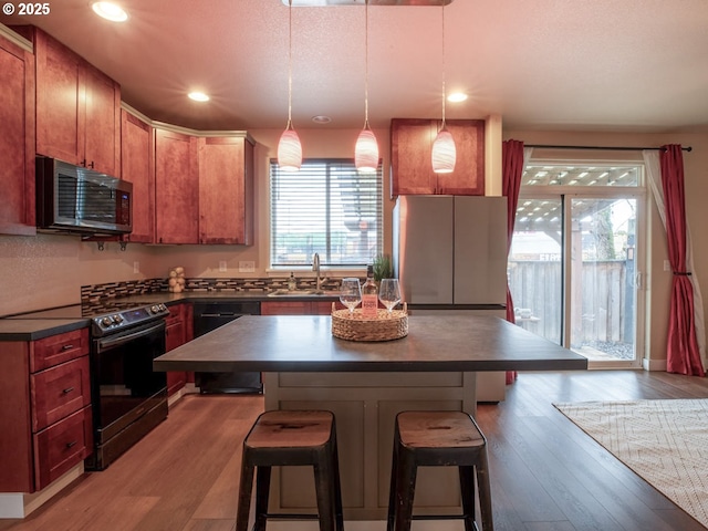 kitchen with sink, light hardwood / wood-style flooring, appliances with stainless steel finishes, a kitchen island, and pendant lighting