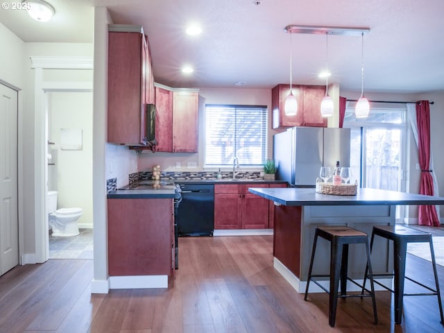 kitchen with stainless steel fridge, dishwasher, hanging light fixtures, a healthy amount of sunlight, and a kitchen island