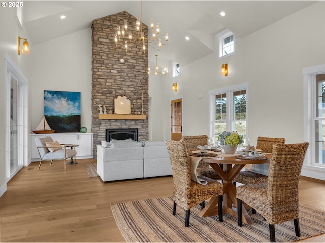 dining area with a chandelier, high vaulted ceiling, a stone fireplace, light wood-style flooring, and recessed lighting