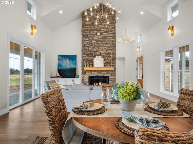 dining space with wood finished floors, a fireplace, high vaulted ceiling, a notable chandelier, and recessed lighting