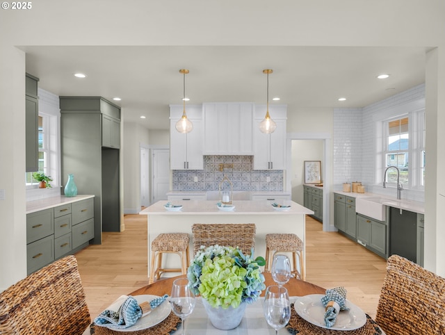 kitchen with a sink, light wood-style floors, white cabinets, light countertops, and decorative light fixtures