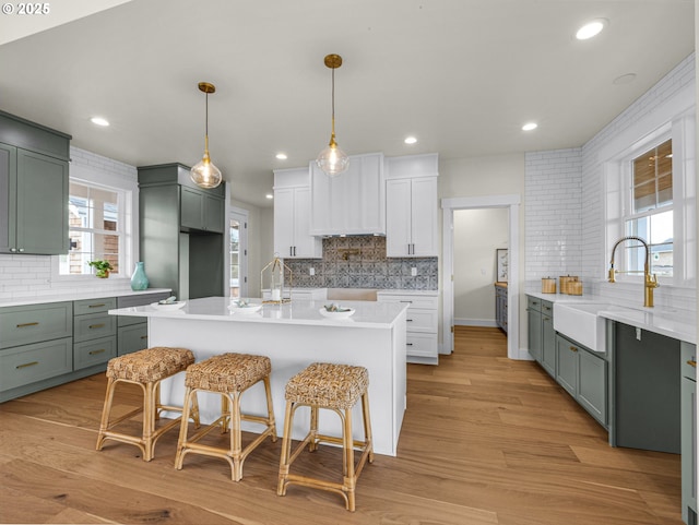 kitchen with a breakfast bar, a sink, light countertops, light wood finished floors, and tasteful backsplash