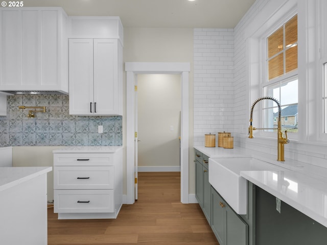 kitchen featuring tasteful backsplash, light wood-style flooring, light countertops, white cabinetry, and a sink