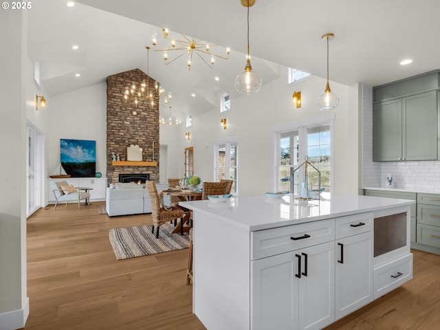 kitchen featuring light wood-style flooring, a center island with sink, light countertops, and a fireplace