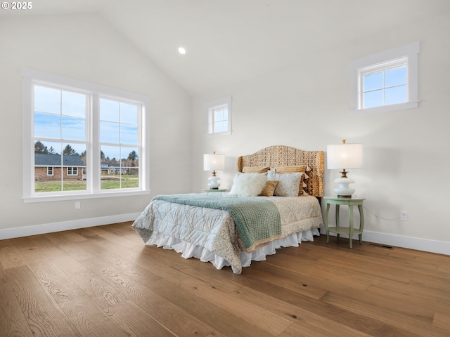 bedroom with lofted ceiling, multiple windows, baseboards, and wood finished floors