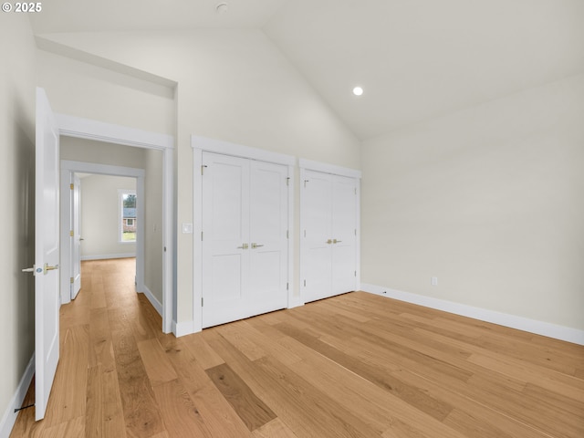 unfurnished bedroom with high vaulted ceiling, recessed lighting, baseboards, light wood-style floors, and two closets