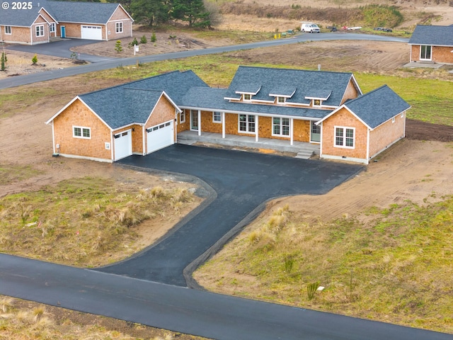 view of front of house with an attached garage, aphalt driveway, roof with shingles, and a porch