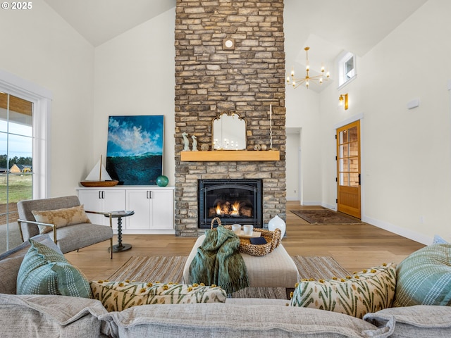 living area featuring light wood-style flooring, a chandelier, high vaulted ceiling, and a stone fireplace