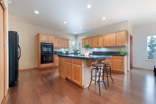 kitchen with dark hardwood / wood-style floors, a breakfast bar, a center island, black appliances, and light brown cabinets