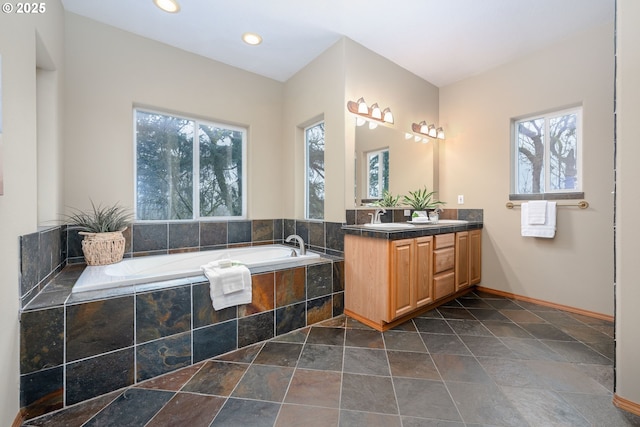 bathroom with a relaxing tiled tub, vanity, and a healthy amount of sunlight