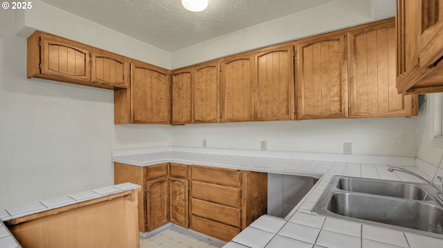 kitchen with sink, a textured ceiling, and tile counters