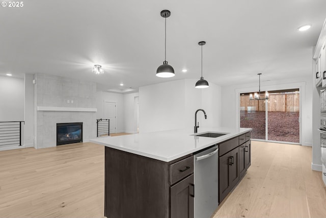 kitchen featuring dishwasher, an island with sink, sink, dark brown cabinetry, and light hardwood / wood-style floors