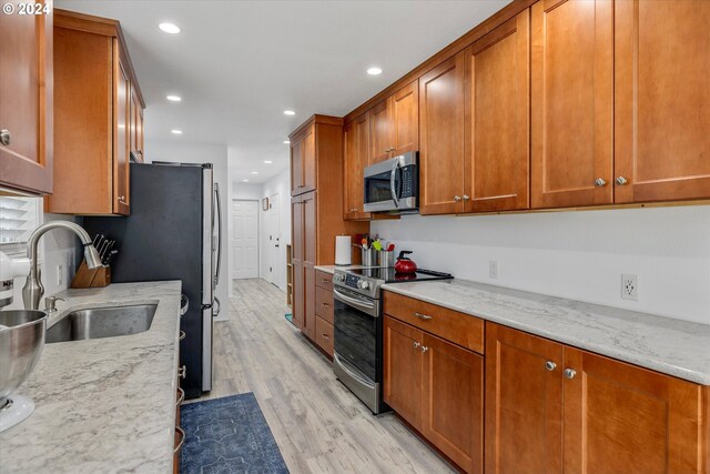 kitchen with light stone countertops, sink, light wood-type flooring, and appliances with stainless steel finishes