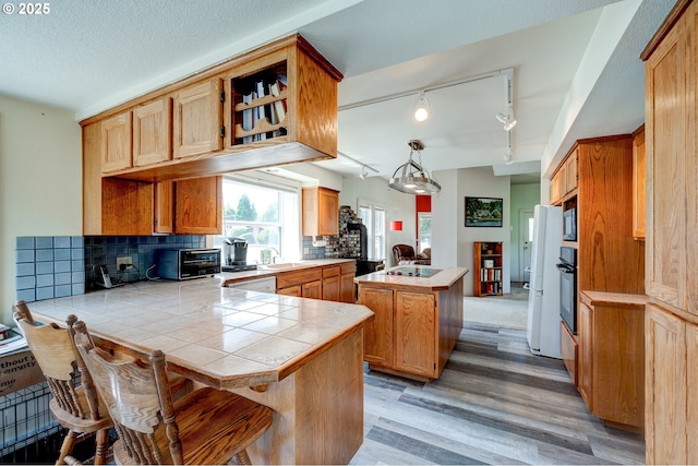 589 NW 3rd Ave, Canby, OR 97013 - kitchen featuring a peninsula, track lighting, light wood-style flooring, tile countertops, and decorative backsplash