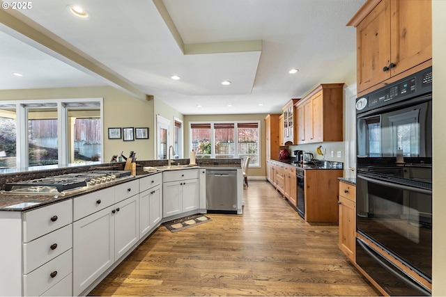 kitchen with sink, dark stone countertops, appliances with stainless steel finishes, light hardwood / wood-style floors, and white cabinets