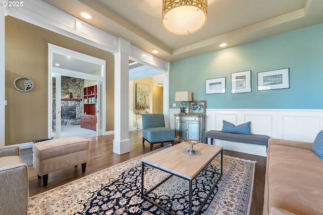 living room featuring a tray ceiling, a fireplace, decorative columns, and wood-type flooring