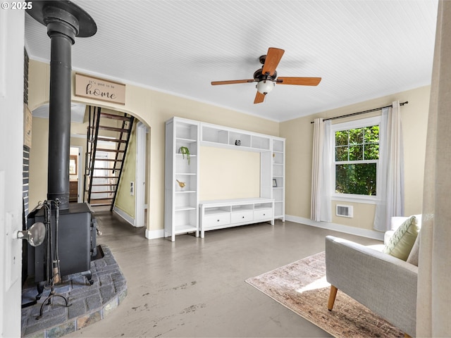 sitting room with baseboards, concrete floors, ceiling fan, and a wood stove