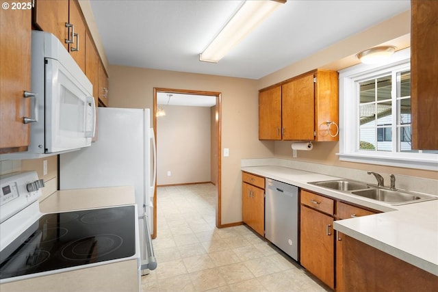 kitchen with light floors, light countertops, brown cabinetry, a sink, and white appliances