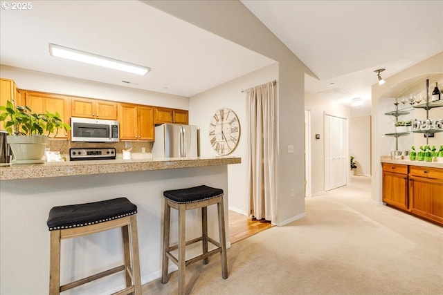 kitchen featuring light countertops, a kitchen bar, light carpet, decorative backsplash, and appliances with stainless steel finishes