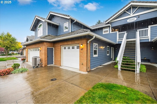 view of front of house featuring brick siding, stairs, cooling unit, a garage, and driveway