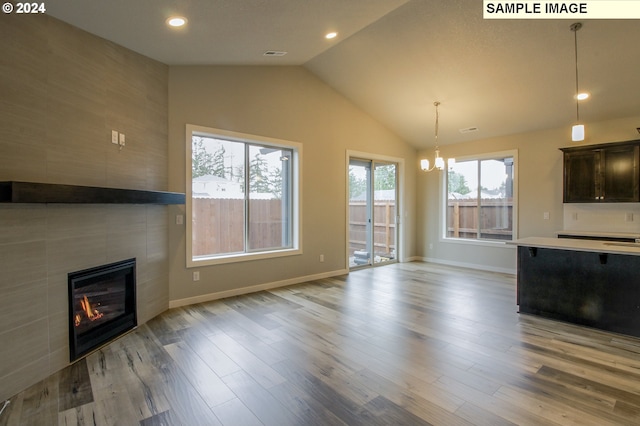 unfurnished living room with a tiled fireplace, vaulted ceiling, a notable chandelier, and light hardwood / wood-style floors