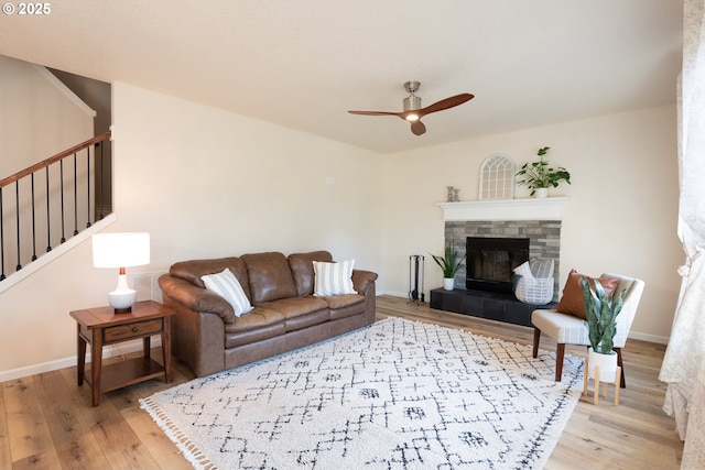 living room with a ceiling fan, a tiled fireplace, light wood-type flooring, baseboards, and stairs