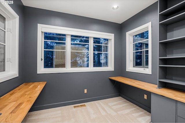 unfurnished office featuring visible vents, built in shelves, baseboards, light colored carpet, and built in study area