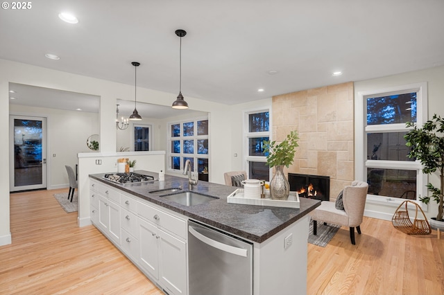 kitchen with light wood finished floors, a fireplace, a sink, white cabinets, and appliances with stainless steel finishes