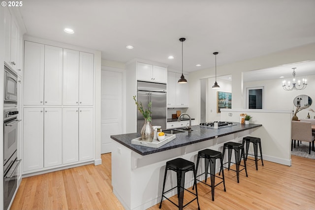 kitchen featuring a sink, built in appliances, white cabinetry, a kitchen breakfast bar, and light wood-type flooring