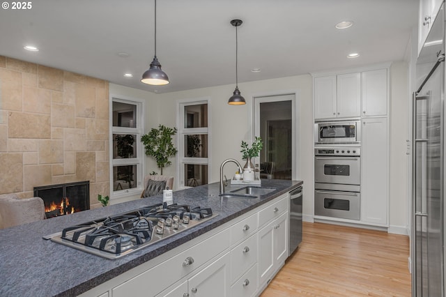 kitchen featuring a tile fireplace, a sink, white cabinets, appliances with stainless steel finishes, and light wood-type flooring